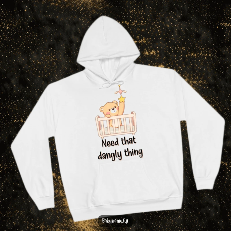 Funny teddy bear in a crib eagerly reaching for a hanging mobile, capturing adorable curiosity. A cozy, humorous hoodie.