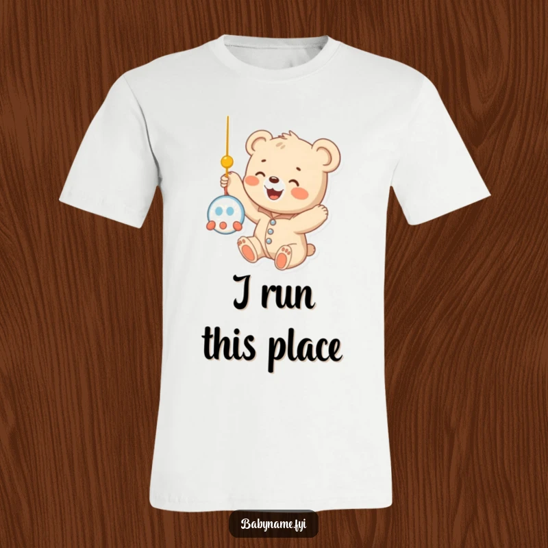 Funny baby bear cub wearing a soft onesie, reaching out with tiny paws towards a colorful dangling mobile, looking absolutely adorable on a t-shirt.