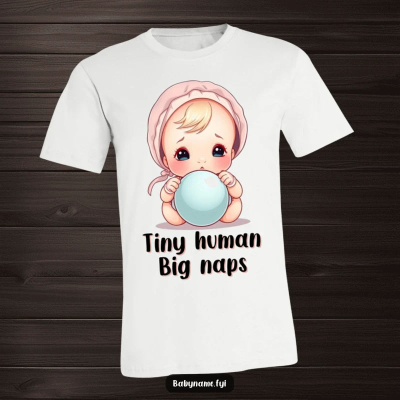 Funny baby wearing a tiny bonnet, peeking mischievously over a rattle, a cute and funny t-shirt.