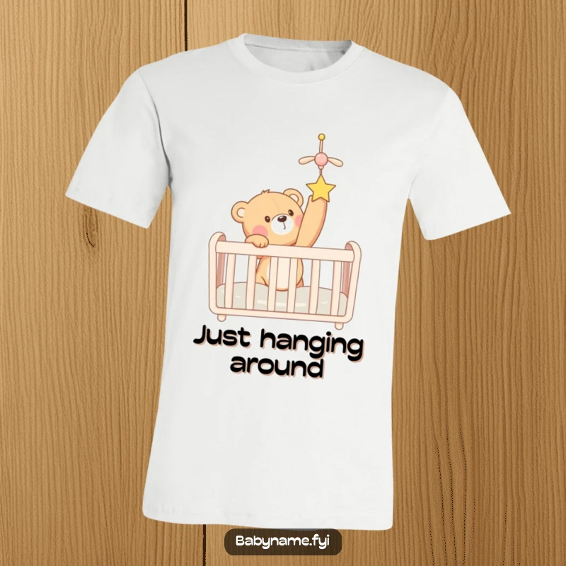 Funny teddy bear character in a crib stretching to grab a dangling mobile, expressing pure glee. A cute, humorous apparel.